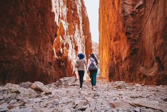 Two hikers walking through a narrow red rock canyon on a rocky trail