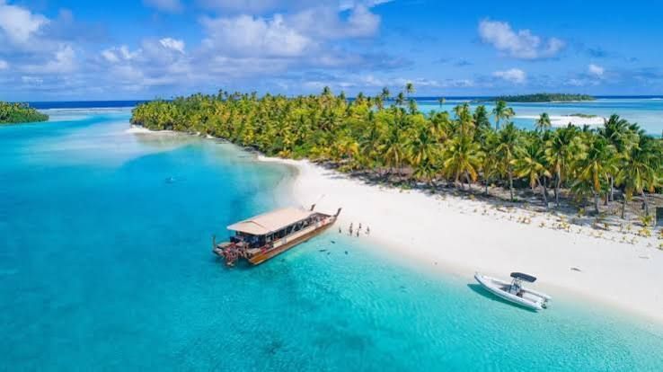 Tropical beach with turquoise water, palm trees, and a small boat docked on white sand