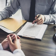 A man is sitting at a table signing a document with a pen.