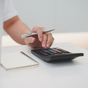 A person is using a calculator and holding a pen.