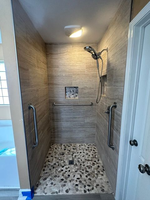Accessible walk-in shower with pebble floor, grab bars, and handheld showerhead indoors