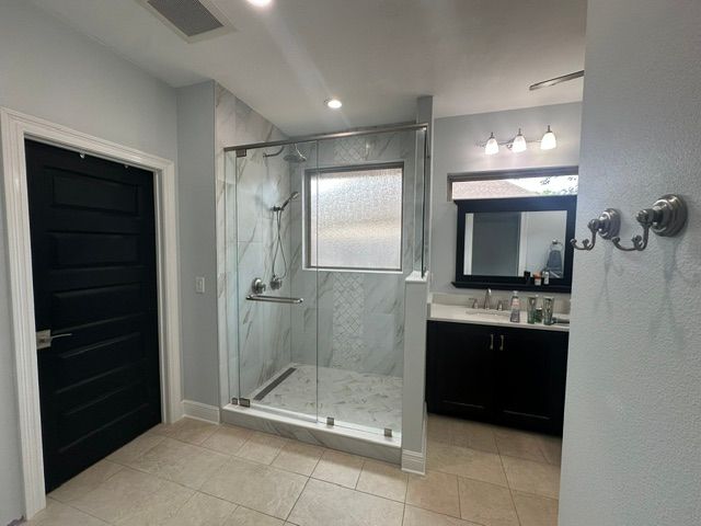 Modern bathroom with walk-in shower, black door, and double-sink vanity with mirror.