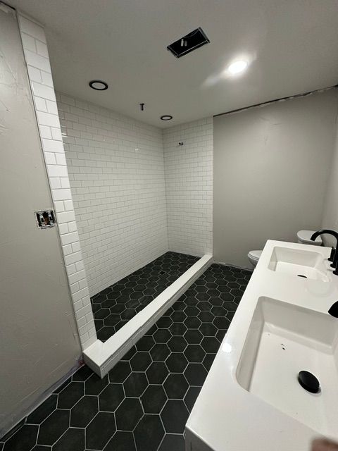 Public restroom with two white sinks, gray stall doors, and a white-tiled shower area with black hex floor.