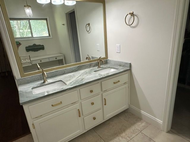 Bathroom vanity with marble countertop, gold-framed mirror, and double sinks in a bright room
