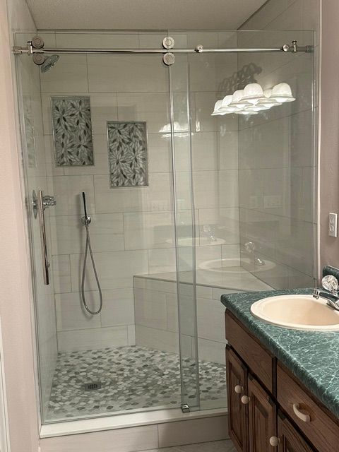 Glass-enclosed tiled shower with pebble floor, rainfall showerhead, and bathroom vanity sink visible.