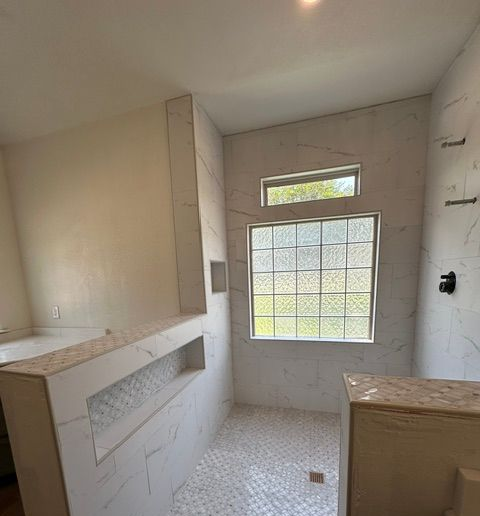 Small unfinished bathroom with tiled walls, frosted window, and a countertop over a sink area.