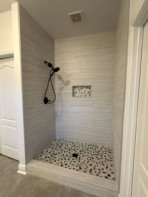 Bathroom shower stall with tiled walls, black shower fixture, and black-and-white pebble floor.