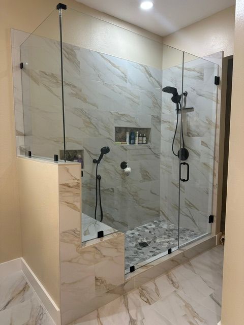 Modern bathroom shower with glass enclosure, marble tile walls, dual showerheads, and pebble-stone floor.