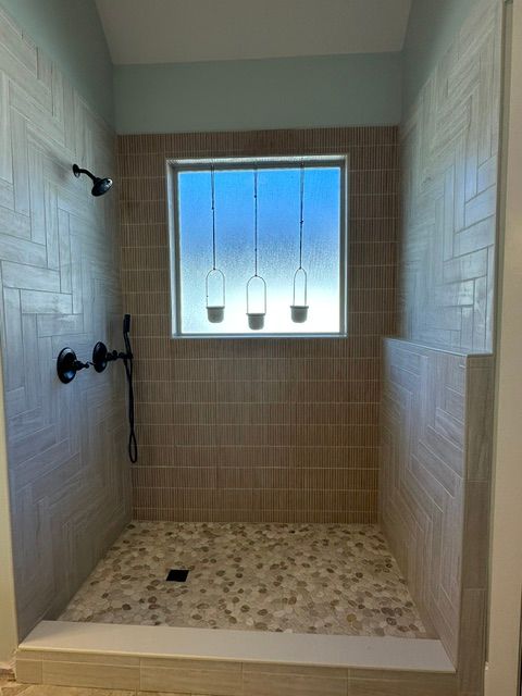 Walk-in shower with white stone walls, pebble floor, and three pendant lights at the window.