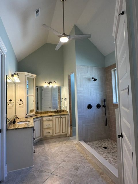 Spacious bathroom with walk-in shower, double vanity, and high vaulted ceiling with ceiling fan