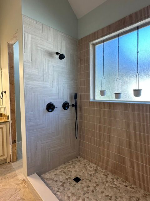 Modern walk-in shower with marble walls, pebble floor, black fixtures, and a frosted window with pendant lights.