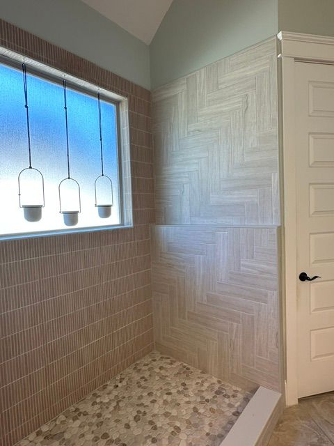 Empty bathroom with tiled walls, a patterned bench, and three hanging pendant lights by a window.