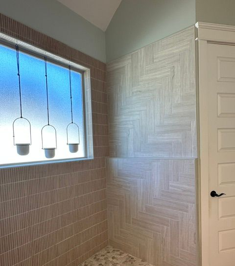 Bathroom with a tiled walk-in shower, frosted window, and three pendant lights over the tub area