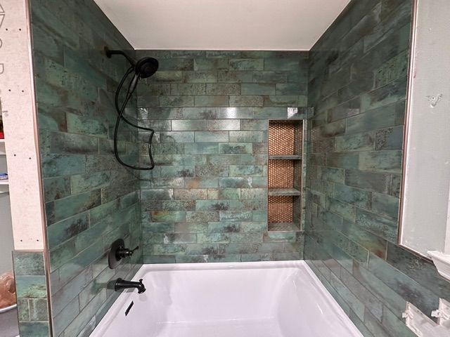 Modern bathroom with green tile walls, white bathtub, black shower fixtures, and a recessed shelf niche