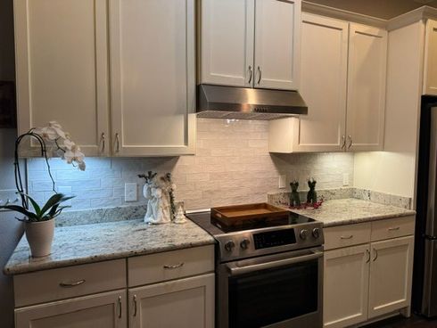 Modern kitchen with white cabinets, granite countertops, and stainless steel stove under a range hood