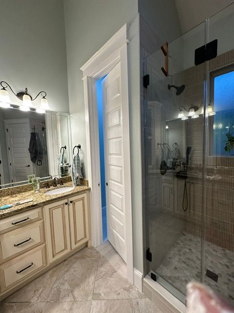 Bathroom vanity with granite countertop and large glass shower enclosure, lit by vanity lights.