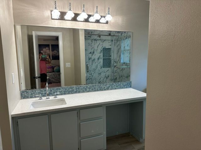 Bathroom vanity with mirror, white countertop, gray cabinets, and blue tile backsplash