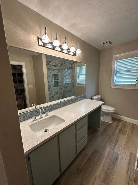 Modern bathroom with double vanity, large mirror, gray cabinets, white countertop, toilet, and window blinds.