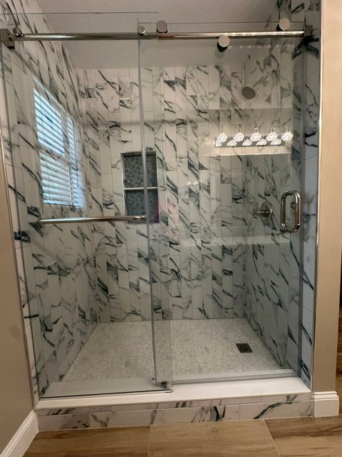 Marble-tiled glass shower enclosure with sliding door and built-in bench in a bathroom