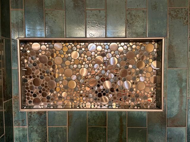 Decorative pebble mosaic wall art inset in a teal tile wall, lit warmly