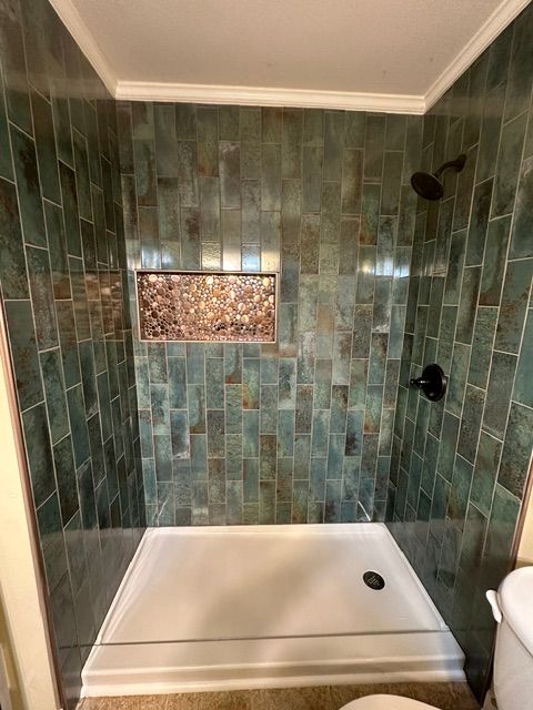 Small tiled bathroom shower with green walls, white tub, and mosaic accent inset.