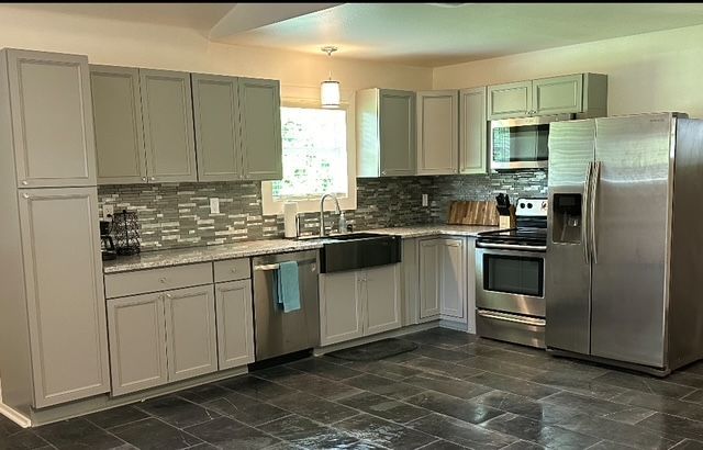 Modern kitchen with white cabinets, stainless steel appliances, and dark tile flooring