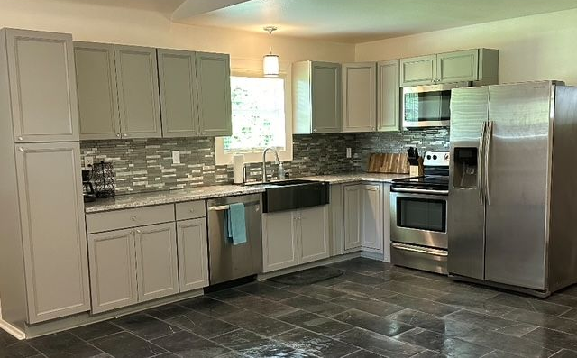 Modern kitchen with light cabinets, stainless steel appliances, gray tile backsplash, and dark floor tiles