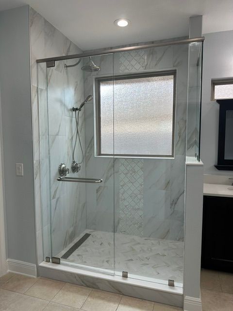Glass-enclosed walk-in shower with marble-look tile, grab bars, shower bench, and frosted window