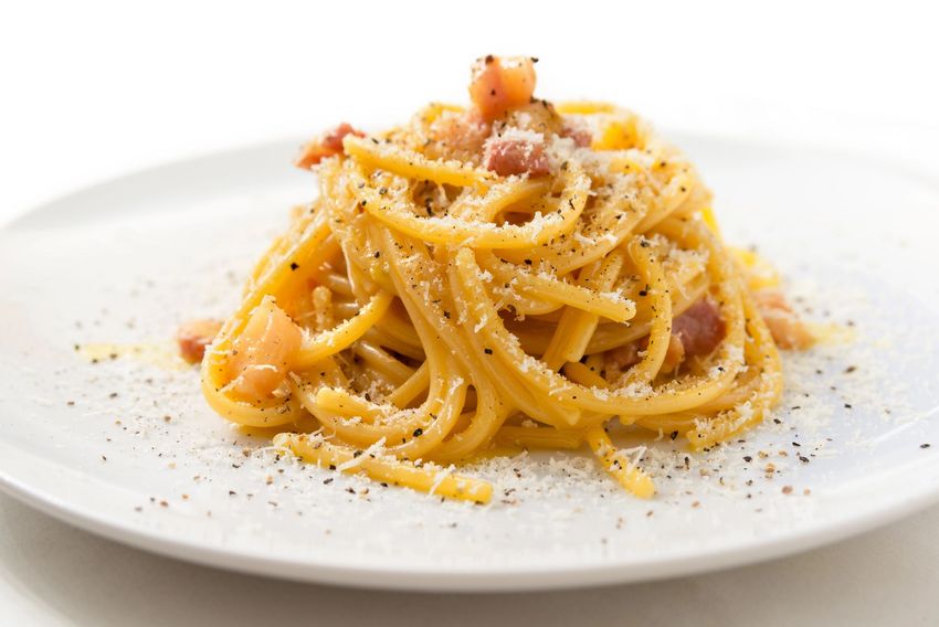 Pasta alla carbonara su un piatto bianco, condita con formaggio grattugiato e pepe.