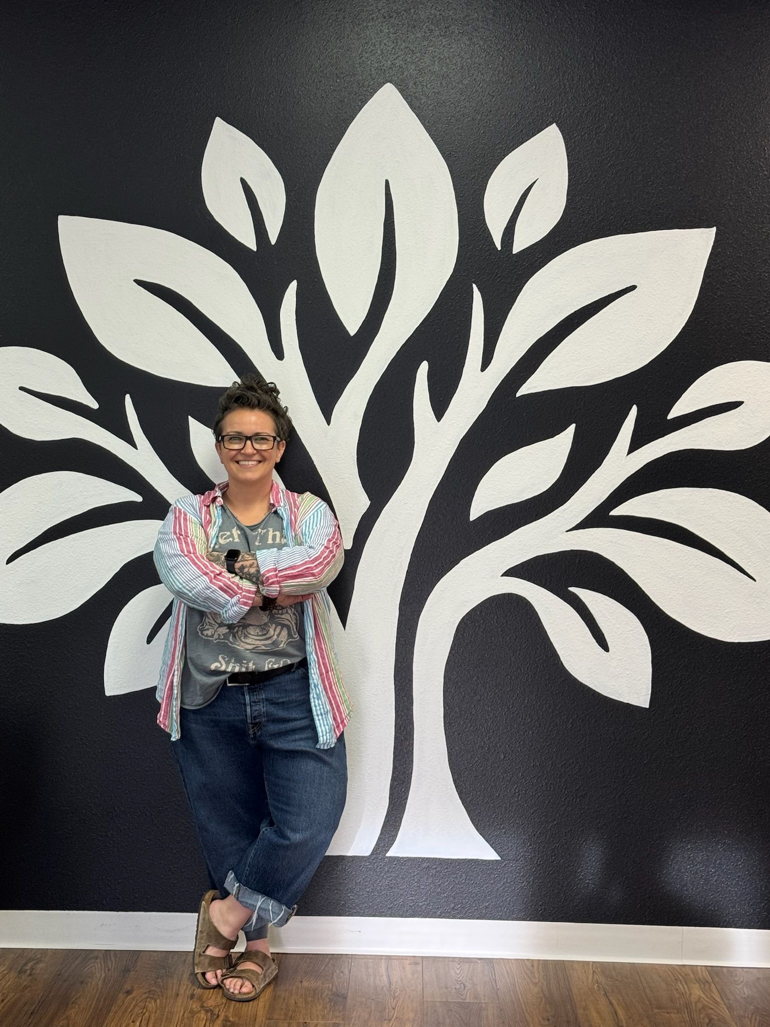 Christen Spain standing against a wall with the Fayetteville School of Massage logo painted on the wall.