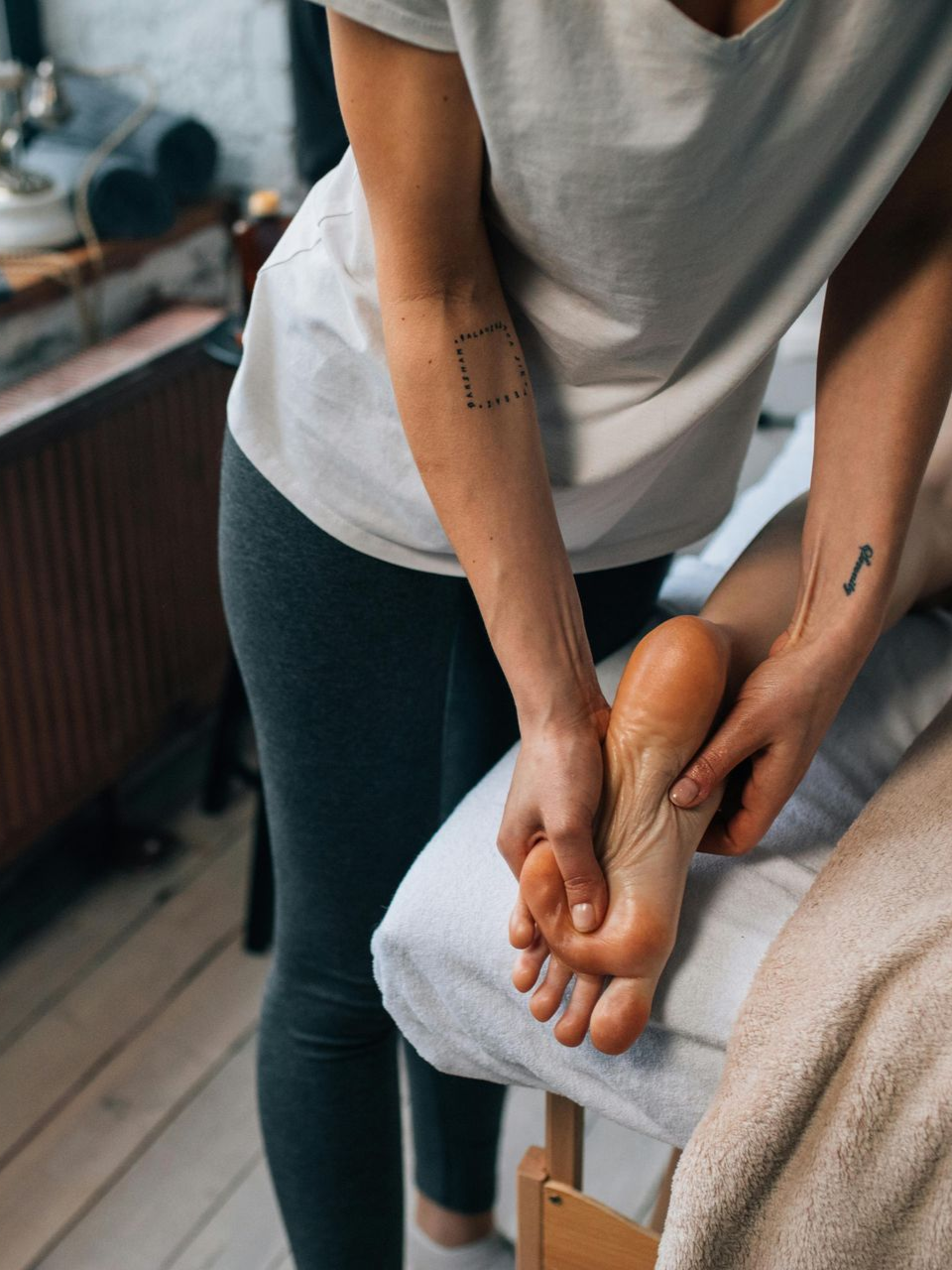 Person giving a foot massage to a client on a treatment table in a cozy room
