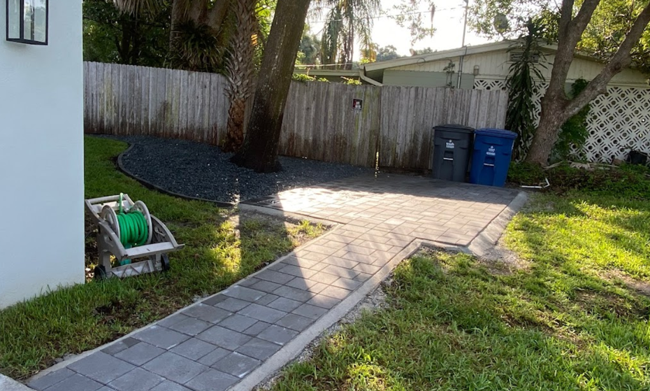 A walkway leading to a backyard with a fence and trash cans.