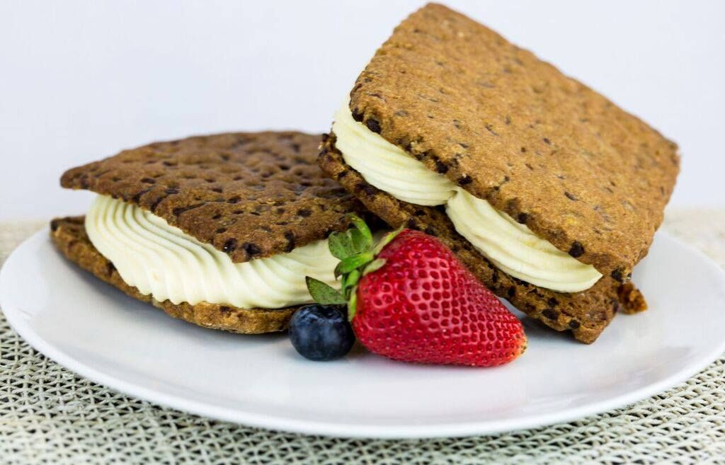 Two ice cream sandwiches on a plate with strawberry and blueberry.