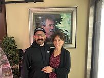 A man and a woman are posing for a picture in front of a painting of a man.