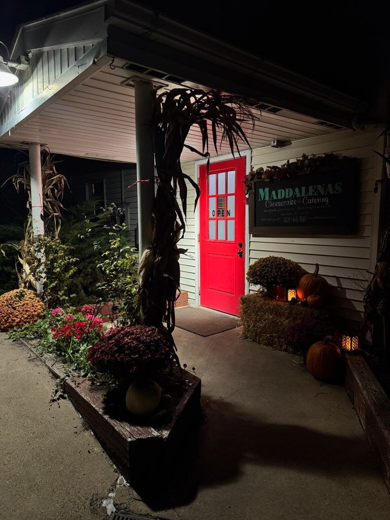 Red door entrance to Madalyn's restaurant, decorated with fall pumpkins and flowers, at night.