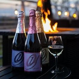 Three bottles of sparkling wine and a glass of wine on a table in front of a fire pit.