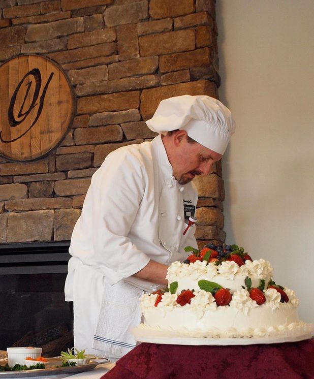 A chef prepares a cake with strawberries and whipped cream