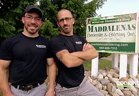 Two men are standing in front of a sign for maddales cheesecake shop
