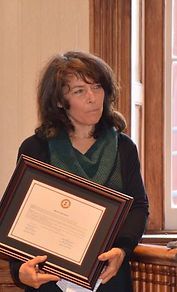 A woman is holding a framed certificate in front of a window.