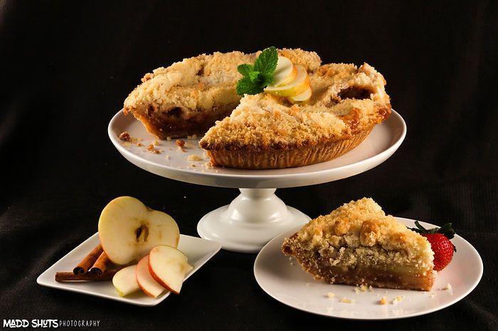 A slice of apple pie is on a plate next to an apple pie on a cake stand.