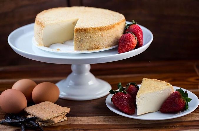 A cheesecake on a cake stand with strawberries on a plate
