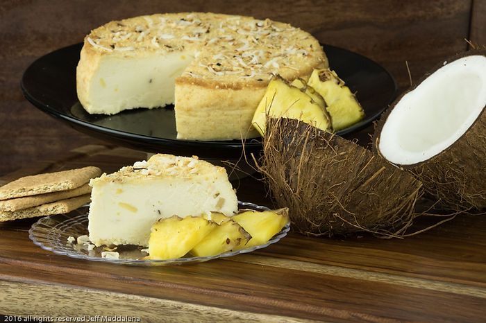 A piece of cheesecake is on a plate next to a coconut and pineapple slices.