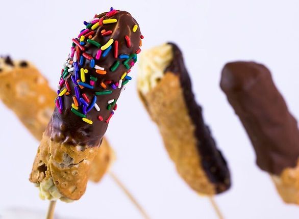 Cannoli pops dipped in chocolate with sprinkles, close-up on a white background.