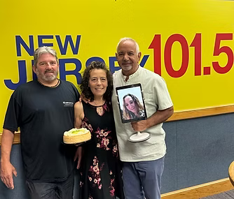 Three people are posing for a picture in front of a yellow wall that says new jersey 101.5