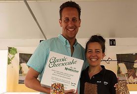 A man and a woman are standing next to each other holding a box of classic cheesecake.
