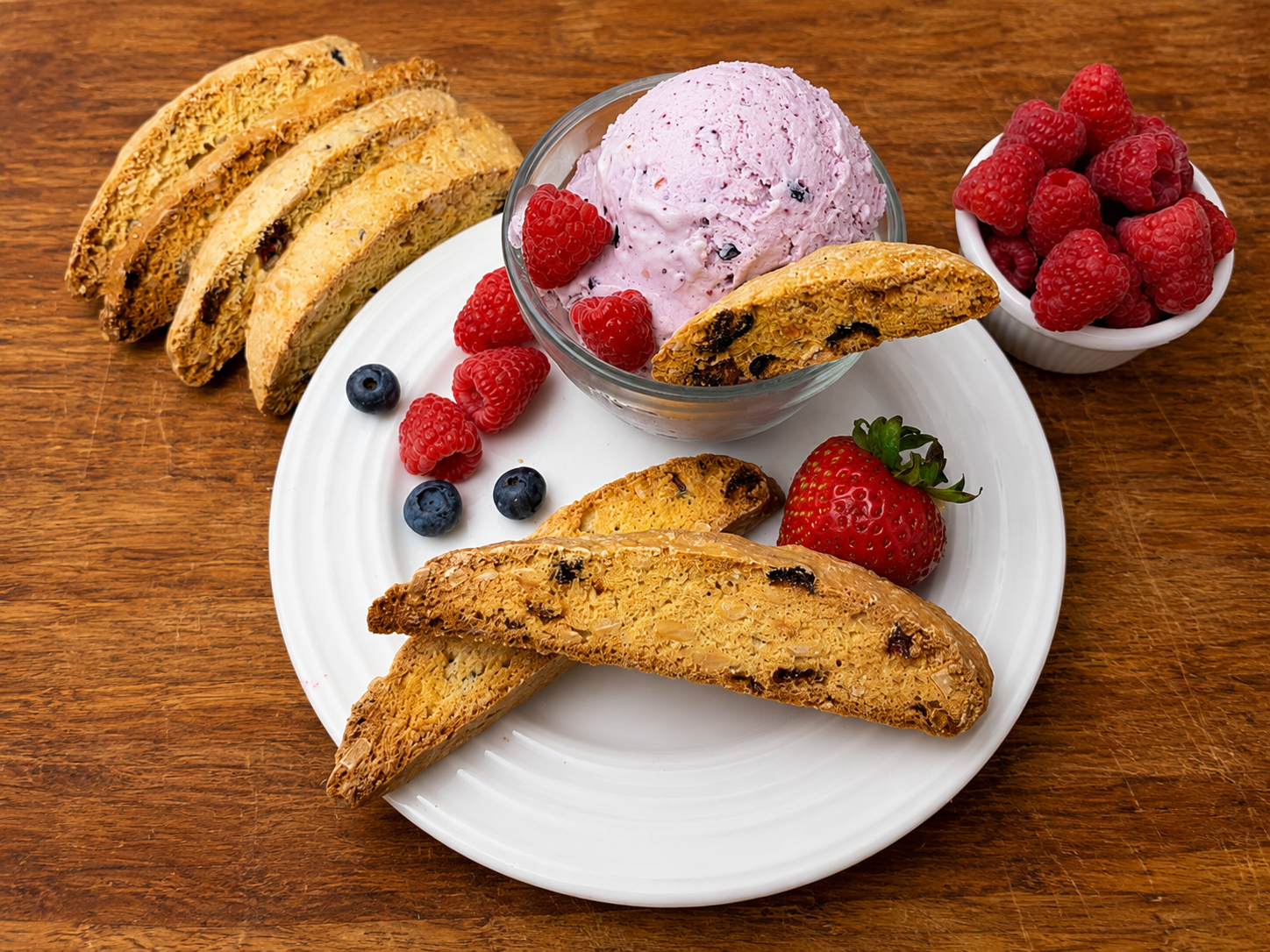 Dessert plate with crepe rolls, berries, and pink ice cream on a wooden table