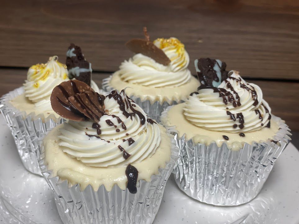 Four cupcakes with white frosting and chocolate sprinkles on a white plate.