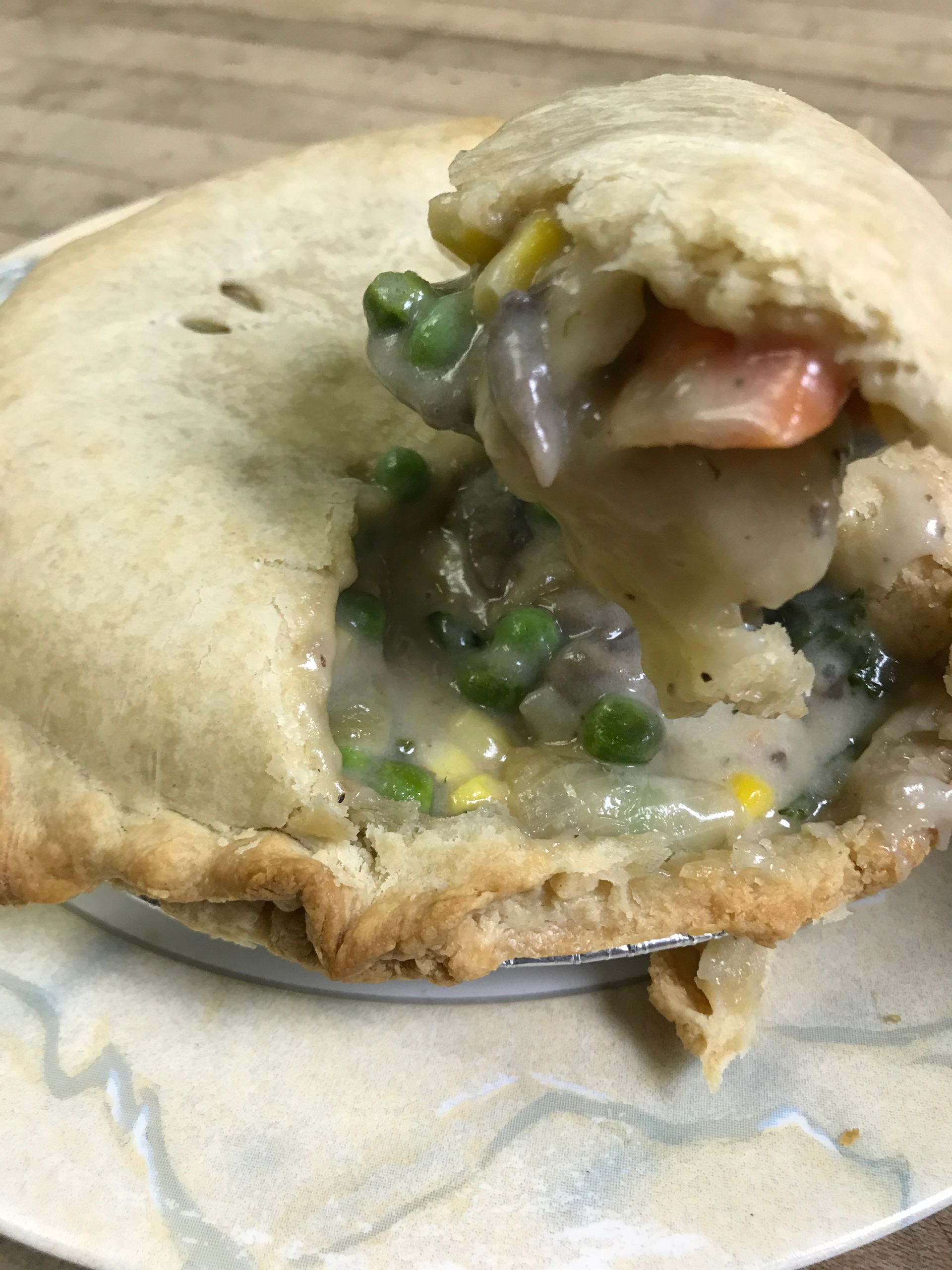 Chicken pot pie, crust broken open, showing filling of vegetables in creamy sauce.