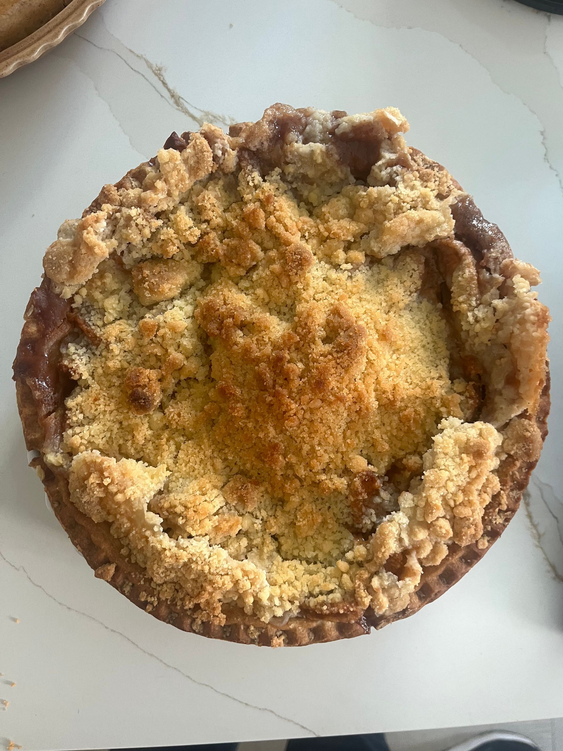 Apple crumble dessert on a white countertop. Crumble topping is golden brown, and filling is visible.