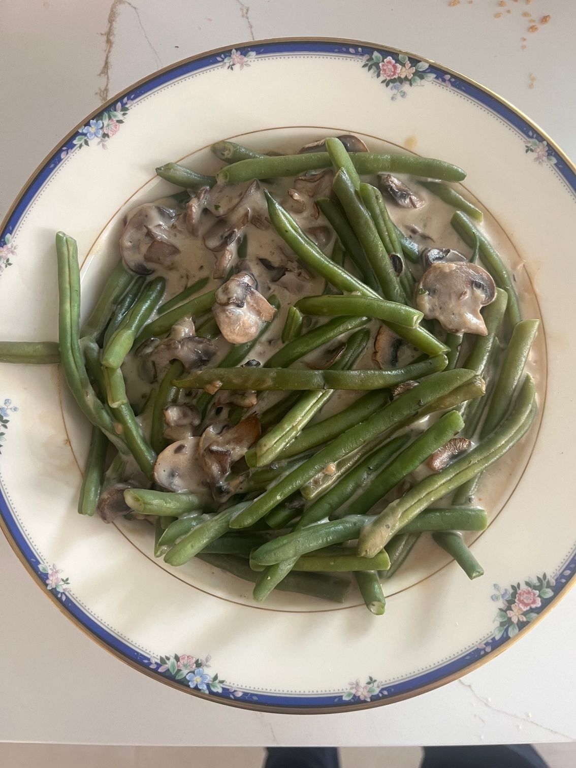 Green beans and mushroom dish in creamy sauce on a decorative plate.
